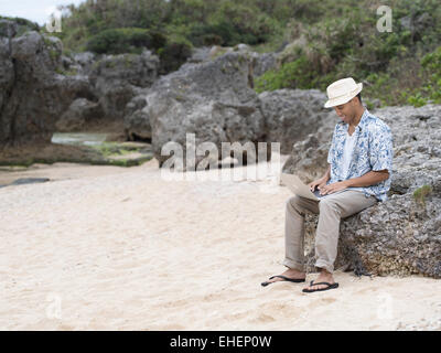Mann mit Apple Macbook Air-portable Laptop-Computer am Strand im Urlaub arbeiten Stockfoto