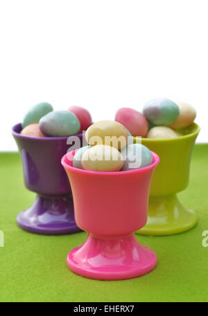 Eierbecher gefüllt mit kleinen Ostereiern auf grünem und weißem Hintergrund Stockfoto
