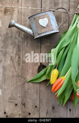 Metall kleine Gießkanne mit Herz hing an einer Schnur auf hölzernen Hintergrund Stockfoto