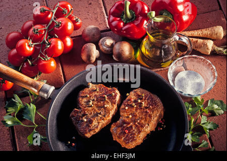 Zwei gebratener Paprika Steaks in einer Pfanne, Dekoration mit frischen Tomaten, Pilze, Sellerie und rote Paprika, auf Terracotta Fliesen Stockfoto