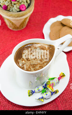 Tasse Kaffee mit Bonbons und Kekse auf einer roten Tischdecke Stockfoto