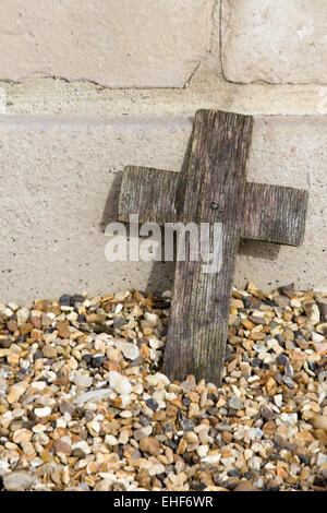 Holzkreuz gegen eine Steinmauer zur Erinnerung in Kies gelegt. Stockfoto