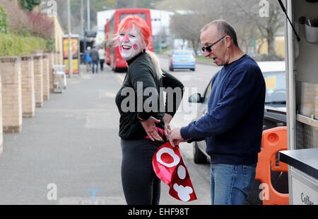 Brighton, UK. 13. März 2015. Kunden Martin Williamson hilft mobilen Café-Besitzer Kim Coghlan mit ihrem Comic Relief Red Nose-Outfit in Brighton Vormittag Credit: Simon Dack/Alamy Live News Stockfoto