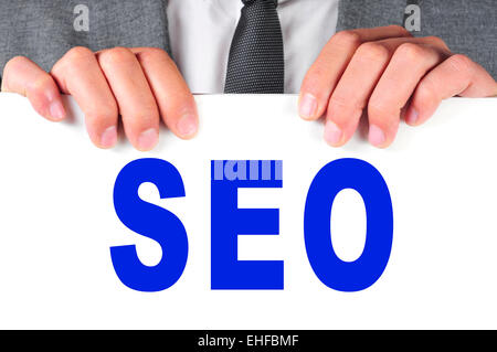 ein Mann in einem Anzug hält ein Schild mit dem Wort SEO, Abkürzung für Search Engine Optimization, geschrieben Stockfoto