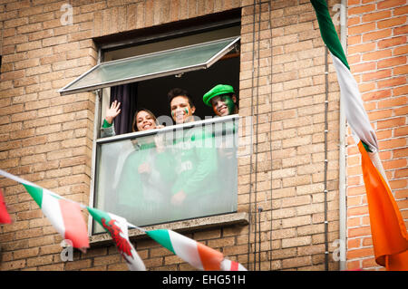 Gruppe von ausländisch aussehenden Menschen in grün gekleidet, mit Gesicht, Lächeln und winken aus dem Fenster in Dublin am St. Patricks Day Stockfoto