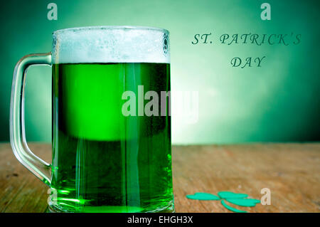 ein Glaskrug mit gefärbten Jungbier und eine dreiblättrige Kleeblatt auf einem Holztisch und den Text St Patricks Tag Stockfoto