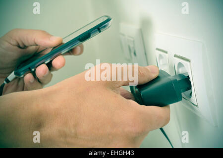 Nahaufnahme von den Händen eines Mannes in seine Smpartphone in eine Steckdose mit einer Filter-Effekt-Stecker einstecken Stockfoto