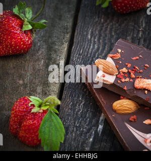 Handgemachte dunkle Schokolade mit Erdbeerscheiben Closeup, frische Beeren auf alten Holztisch Stockfoto
