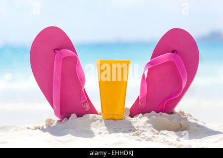 Rosa lebhaften Strand Flip-Flops mit Sonnencreme Schutz Gesichtscreme im weißen Sand am Meer-Hintergrund. Tropischer Sommer Urlaub con Stockfoto