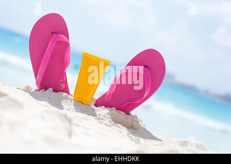 Rosa lebhaften Strand Flip-Flops mit Sonnencreme Schutz Gesichtscreme im weißen Sand am Meer-Hintergrund. Tropischer Sommer Urlaub con Stockfoto