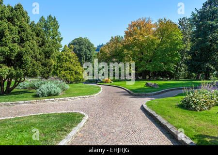 Gepflasterter Weg zwischen grünen Wiesen und üppigen Bäumen von Valentino-Park in Turin, Italien. Stockfoto