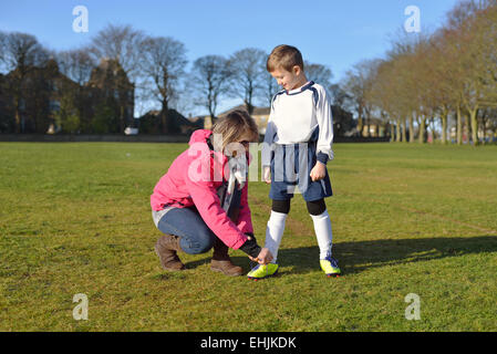 Mutter binden Boot Schnürsenkel eines kleinen Jungen am Fußballplatz. Stockfoto