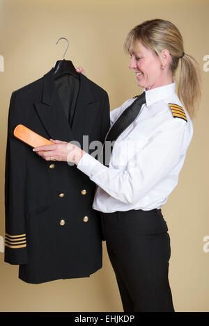 Weibliche Flugkapitän Bürsten Staub aus ihrer Uniformjacke Stockfoto