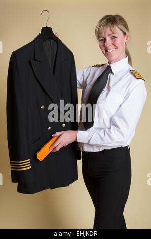 Weibliche Flugkapitän Bürsten Staub aus ihrer Uniformjacke Stockfoto