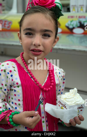 Eine Mädchen in traditioneller Kleidung genießt ein Eis im Fiesta de San Miguel in Orgiva, Andalusien, Spanien Stockfoto