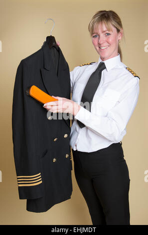 Weibliche Flugkapitän Bürsten Staub aus ihrer Uniformjacke Stockfoto