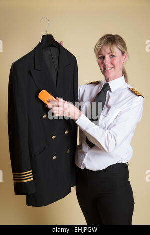 Weibliche Flugkapitän Bürsten Staub aus ihrer Uniformjacke Stockfoto