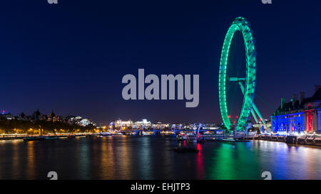 Das London Eye, County Hall und die Skyline von London sind gegen einen nächtlichen Himmel beleuchtet und spiegelt sich in der Themse. Stockfoto