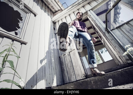 Ein junger Mann Tritte und Rauchen vor einem verlassenen Haus. Stockfoto