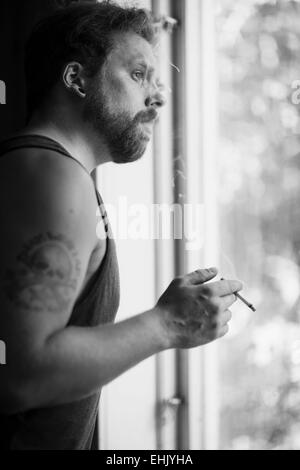 Punk-Rocker am Fenster stehend, Zigaretten rauchen und denken. Stockfoto