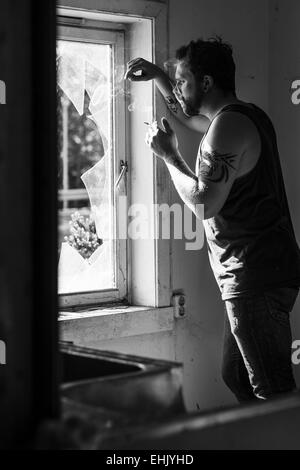 Rocker stehen durch ein zerbrochenes Fenster, Zigaretten rauchen und denken. Stockfoto