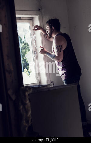 Rocker stehen durch ein zerbrochenes Fenster, Zigaretten rauchen und denken. Stockfoto