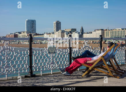 Touristen sitzen auf Liegestühlen am Pier von Brighton Stockfoto