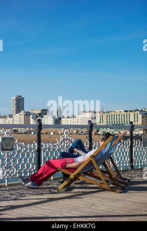 Touristen sitzen auf Liegestühlen am Pier von Brighton Stockfoto