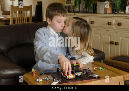 Junge, acht Jahre alt, mit Schwester, spielen zwei Jahre alt, mit Lego zusammen. Mädchen küssen Junge, aber er spielt beschäftigt, UK. Stockfoto