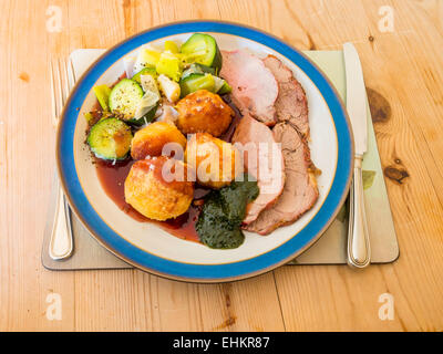 Englisch Braten Mittagessen am Sonntag Lamm Brokkoli Lauch und Soße serviert mit Minze-Sauce auf einem blau-weißen Platte Holztisch Stockfoto