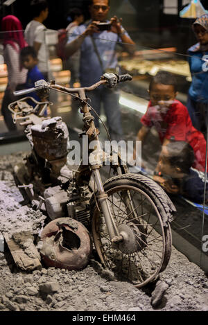 Bandung, Indonesien. 15. März 2015. Kinder zu beobachten, dass ein beschädigtes Motorrad getroffen pyroklastische Ströme, Geologie-Museum, Bandung, Indonesien. Das Artefakt stammt von 2010 Mount Merapi Ausbruch Website in Yogyakarta Provinz. Stockfoto