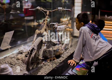 Bandung, Indonesien. 15. März 2015. Kinder zu beobachten, dass ein beschädigtes Motorrad getroffen pyroklastische Ströme, Geologie-Museum, Bandung, Indonesien. Das Artefakt stammt von 2010 Mount Merapi Ausbruch Website in Yogyakarta Provinz. Stockfoto