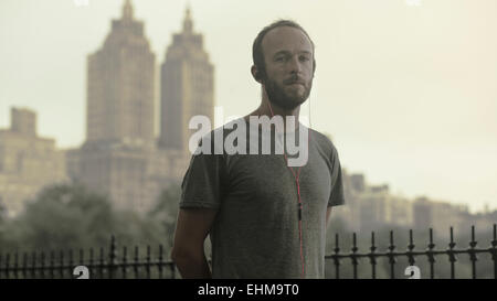 Kaukasische Läufer anhören Ohrhörer vor der Skyline der Stadt Stockfoto