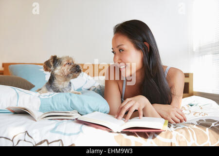 Chinesin mit Hund auf Bett entspannen Stockfoto