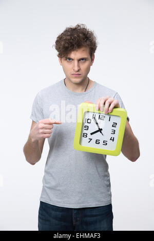 Zorniger junger Mann mit lockigem Haar zeigt auf die Uhr Stockfoto