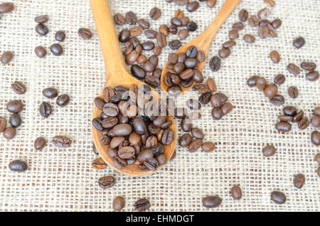 Große und kleine Löffel gefüllt mit ganzen Kaffeebohnen auf einem Vintage Tischdecke Stockfoto