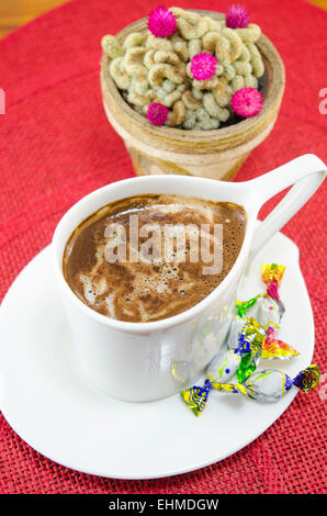 Tasse Kaffee mit Bonbons und ein Kaktus im Hintergrund Stockfoto