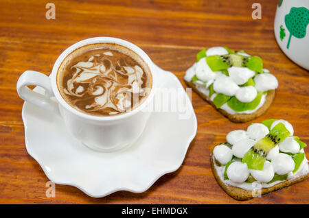 Tasse Kaffee mit dekorierten Schaum und Kiwi mit Creme Kekse Stockfoto