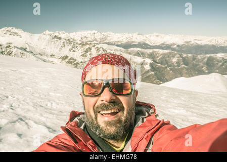 Erwachsenen europäischen Mann unter Selfie auf verschneiten Hang mit schönen schneebedeckten Alpen im Hintergrund. Getönten Bild, alte r Stockfoto