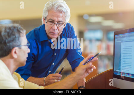 Lehrer helfen Erwachsenen Verwendung Kursteilnehmercomputer in Bibliothek Stockfoto