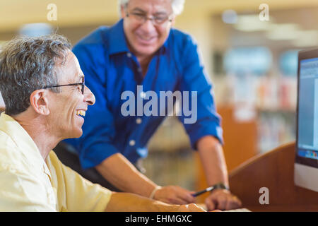 Lehrer helfen Erwachsenen Verwendung Kursteilnehmercomputer in Bibliothek Stockfoto