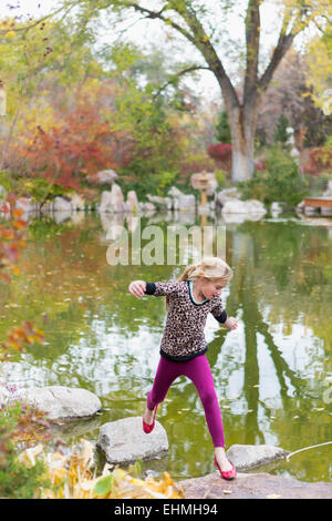 Kaukasische Mädchen springen auf Felsen im Teich Stockfoto