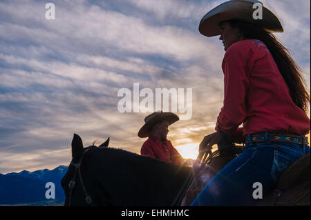 Kaukasische Mutter und Sohn Reitpferde bei Sonnenuntergang Stockfoto