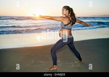 Hispanic schwangere üben Yoga am Strand Stockfoto