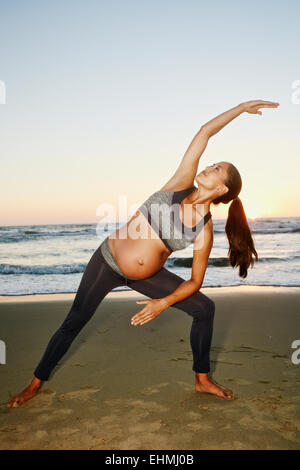 Hispanic schwangere üben Yoga am Strand Stockfoto