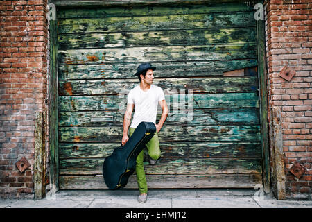 Gemischte Rassen Musiker halten Gitarrenkoffer in der Nähe von Industriegebäude Stockfoto