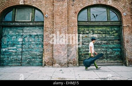 Gemischte Rassen Musiker Gitarre Tragetasche auf Bürgersteig Stockfoto