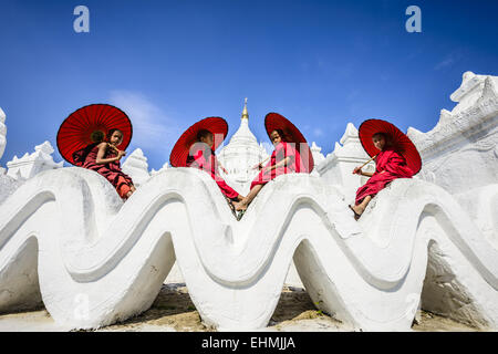 Asiatische Mönche sitzen unter Sonnenschirmen am historischen Tempel, Mingun, Mandala, Myanmar Stockfoto