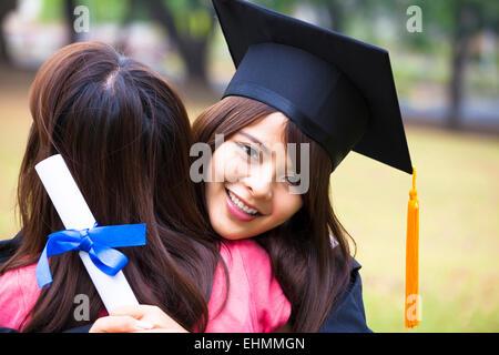 junge weibliche Absolventin umarmt ihre Freundin bei Abschlussfeier Stockfoto