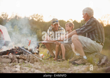 Drei Generationen von kaukasischen Männer Hotdogs über Lagerfeuer rösten Stockfoto